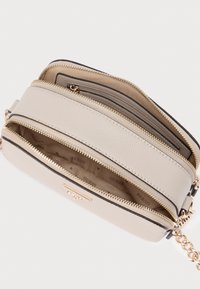 Κομψή μπεζ τσάντα με υφασμένη εξωτερική επιφάνεια, πολλούς θύλακες με φερμουάρ και εξαρτήματα σε χρυσό τόνο. Στο εσωτερικό διαθέτει επένδυση με σχέδιο λογότυπου.