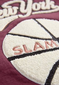 Bordeauxroter Stoff mit einem gestickten Basketball-Design. Text "SLAM" in pinkem Faden auf einem strukturierten weißen Hintergrund mit schwarzen Umrissen.