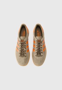 Kerged pruuni nahast tossud, millel on kolm oranživat riba, pruunid paelad ja kummist tald. Iseärasus on oranž logo keele peal.