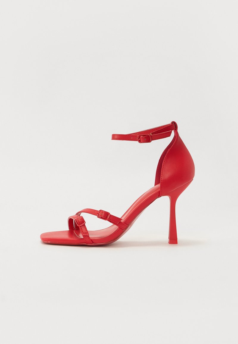 Sandale à talons hauts rouges en cuir lisse et brillant, avec plusieurs fines brides, une boucle à la cheville et un design à bout pointu.