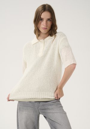 Knit short-sleeve sweater in off-white with a collared neck, featuring a loose fit, textured weave, and ribbed hem. Paired with light gray jeans.
