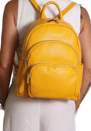 Sac à dos en cuir jaune avec une surface texturée, doté de trois compartiments zippés et de deux poches latérales. Présenté de dos.