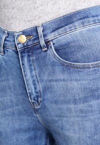 Jeans de mezclilla azul claro con un diseño clásico de cinco bolsillos, con cierre de botón metálico y costuras visibles.
