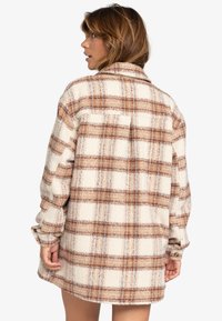 Grote tartan shirt in crèmekleur, bruin en blauw. Heeft een zachte, gestructureerde stof, lange mouwen en een achterste schouderpas met een zak.