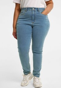 Vaaleansiniset, korkeavyötäröiset farkut, joissa on slim fit -malli. Edessä nappikiinnitys, vyölenkit ja sivutaskut. Silkkinen denimituntu.