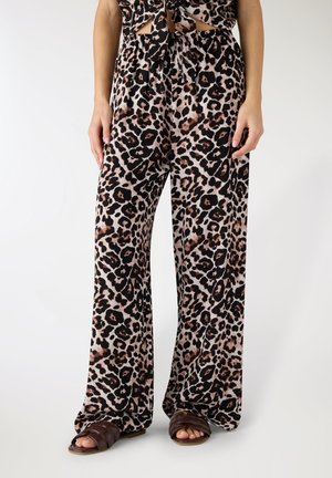 Pantaloni a gamba larga con motivo leopardato nero e marrone, abbinati a sandali neri intrecciati e top coordinato con dettagli ritagliati.