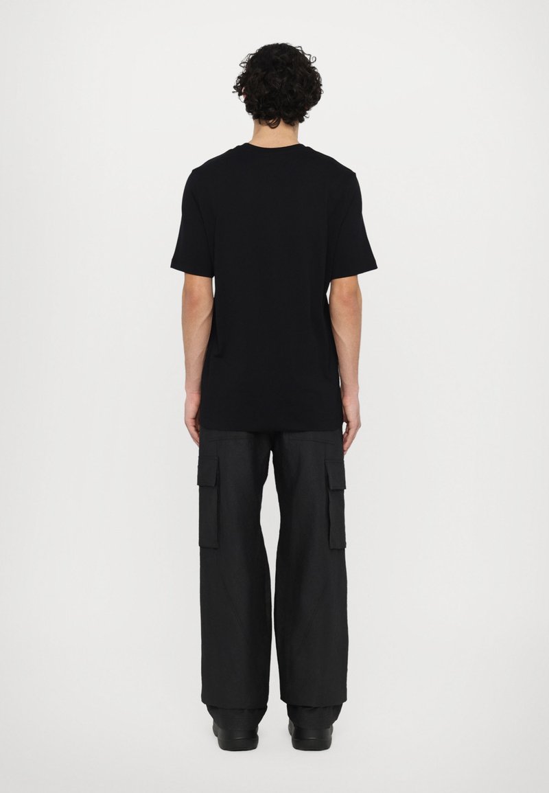 Schwarzes Baumwoll-T-Shirt mit Rundhalsausschnitt und kurzen Ärmeln, kombiniert mit lockeren schwarzen Cargo-Hosen mit Seitentaschen.