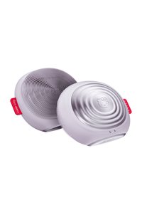 Silicone ansiktsrengöringsapparat i lavendel. Rund form, texturerad sida med fina borst, slät sida med ett cirkulärt mönster. Logotyp synlig.