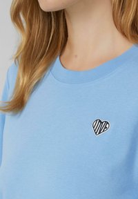 Lichtblauw katoenen sweatshirt met een ronde hals en een klein geborduurd hart met een gestreept patroon in zwart en wit.