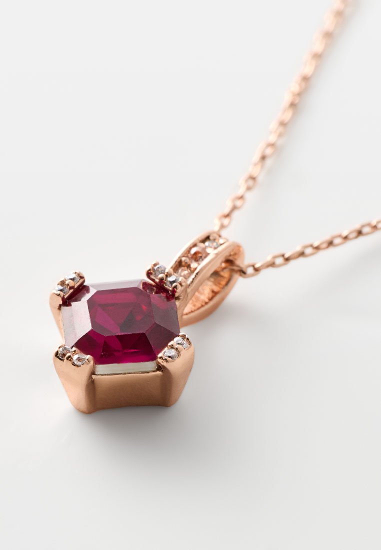 Collana con pendente in oro rosa che presenta una gemma esagonale di un profondo rosso, accentuata da piccole pietre trasparenti su ciascun lato, attaccata a una delicata catena.