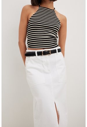 Vrouw draagt een zwart-wit gestreept haltertop, ingestopt in een witte taillehoog rok met een voorkantslits en een zwarte riem.