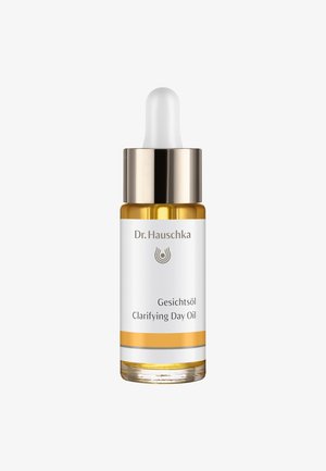 Flacon compte-gouttes en verre brun avec une étiquette blanche. Éléments dorés et argentés, avec le texte "Gesichtöl Clarifying Day Oil" et un design de logo.