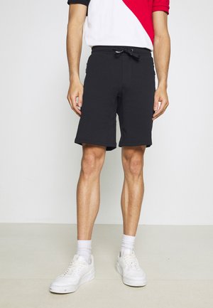 Zwarte katoenen shorts met een elastische tailleband en trekkoord, voorzien van zijzakken met rits en een rechte snit. Gecombineerd met witte sneakers.