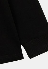 T-shirt noir à manches longues avec des poignets côtelés, texture lisse et design simple. Le tissu semble doux avec un léger éclat.