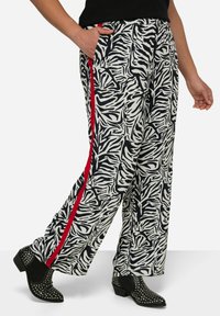 Zwart-wit gestreepte wijde broeken met een zebra-print en rode zijkanten, met een elastische tailleband en zijzakken, gedragen met gestikte zwarte laarzen.