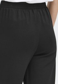 Pantalons de jogging noirs avec une taille élastique, texture de tissu douce et design à jambes larges, présentant une finition lisse et sans motifs visibles.