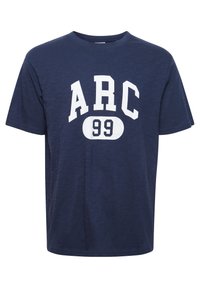 Tumši zila T-kreklu ar īsām piedurknēm, izgatavots no mīkstas kokvilnas, ar lieliem baltajiem uzrakstiem "ARC" un "99" uz priekšpuses. Apaļš izgriezums.