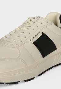 Κρεμ και μαύρο αθλητικό παπούτσι Armani Exchange με κορδόνια, λογότυπο στην πλευρική επιφάνεια και υφασμένο πέλμα σε μακροεντολή.