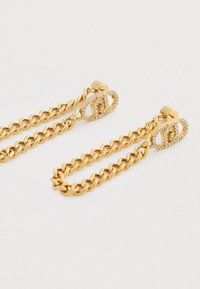 Goldfarbene Kettenohrringe mit einem geflochtenen Design, ausgestattet mit einem funkelnden, ovalen Verschluss, der mit Strasssteinen verziert ist.