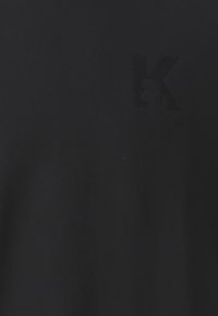 Maglietta nera a maniche corte realizzata in tessuto di cotone liscio, con una delicata lettera "K" in rilievo sul lato sinistro del petto.