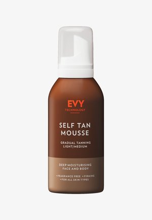 Zelfbruinende mousse in een bruine fles met een witte pompdeksel. Heeft oranje tekst voor branding en productdetails. Geurvrij, geschikt voor alle huidtypes.