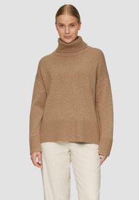 Beige oversized turtlenecktrui van zachte brei met geribde manchetten en zoom, gedragen over crèmekleurige broeken. Gladde textuur met een casual pasvorm.