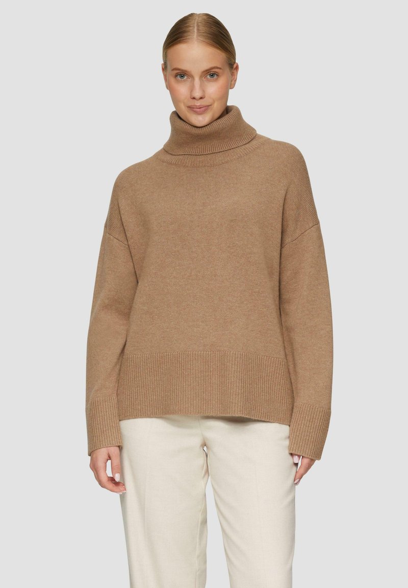 Beige oversized turtlenecktrui van zachte brei met geribde manchetten en zoom, gedragen over crèmekleurige broeken. Gladde textuur met een casual pasvorm.