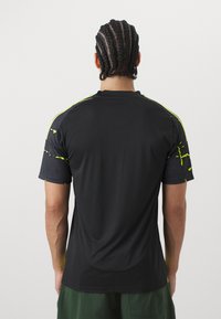 Jersey atlético negro, de manga corta con acentos de malla que presenta un patrón de salpicaduras en verde neón. Elaborado con tejido que absorbe la humedad.