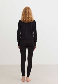 Maglione nero lavorato a maglia con dettagli testurizzati sulle spalle, abbinato a leggings neri. L'outfit è aderente e presenta maniche lunghe.