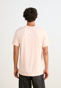 Jasnoróżowa koszulka krótkiego rękawa z okrągłym dekoltem i lekko zaokrąglonym dołem. Miękka tkanina, minimalistyczny design, bez wzorów i akcentów.