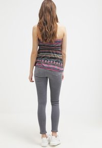 Top de tirantes delgados con estampado multicolor, combinado con jeans ajustados grises y zapatillas blancas. Texturas suaves y diseño ajustado.