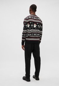 Sweater de Natal preto com rostos brancos de Pai Natal, flocos de neve e padrões geométricos. Usado com calças pretas e sapatos pretos.