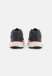 Zapatillas deportivas para hombre con una parte superior oscura, detalles de malla transpirable, acentos rojos y una suela blanca gruesa. Presenta un soporte de talón pronunciado.