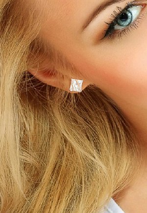 Boucles d'oreilles carrées en argent avec une pierre précieuse transparente dans un motif entrecroisé, sur un fond de cheveux blonds.
