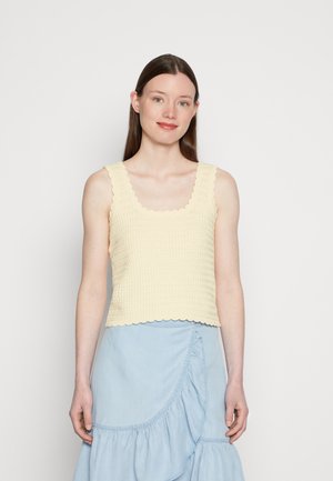 Top de malha em amarelo pálido com um acabamento texturizado, apresentando bordas em forma de onda e alças largas. Combinado com uma saia azul clara, com babados.