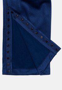 Haine pliabilă albastru marin cu un rând de nasturi negri capsați de-a lungul a două margini, dezvăluind un strat intern moale de țesătură.