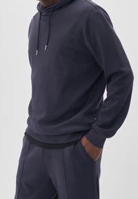 Felpa con cappuccio di colore blu scuro realizzata in tessuto morbido, dotata di cordino, polsini a coste e vita nera. Vestibilità casual con tasche.