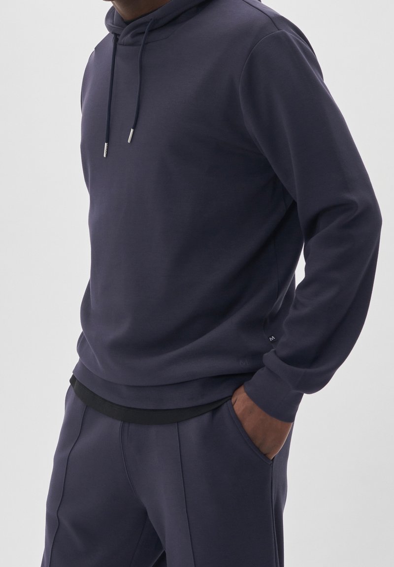 Felpa con cappuccio di colore blu scuro realizzata in tessuto morbido, dotata di cordino, polsini a coste e vita nera. Vestibilità casual con tasche.