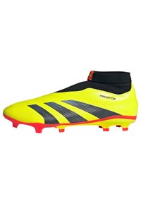 Botines de fútbol color amarillo lima con puño elástico negro en el tobillo, que presentan tres franjas negras, detalles rojos y una superficie texturizada para mejor agarre.