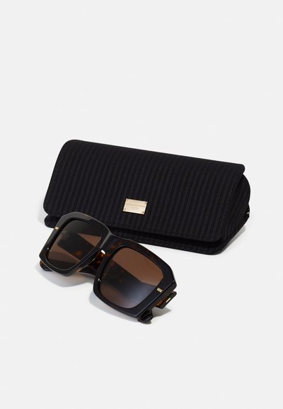 Custodia per occhiali da sole a righe nere con un accento dorato, contenente occhiali da sole oversize in tartaruga con lenti marroni.