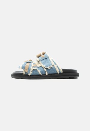 Open-toe sandal with black sole, blue frayed denim straps, and brown buckle closures on a gray background.