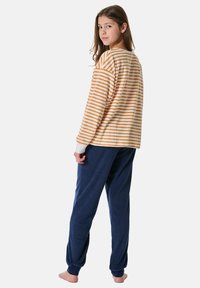 Gestreiftes Langarmhemd in Orange und Weiß, kombiniert mit navyblauen Fleecehosen. Beide Teile haben einen lockeren Schnitt und eine weiche Textur.