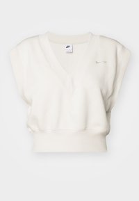 Vit ärmlös Nike-tröja med V-ringning, ribbad struktur och en diskret logga på bröstet. Kort kroppslängd och mjukt tyg.