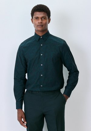 Dark green long-sleeve shirt with a textured leaf pattern, pointed collar, and button closure. Paired with dark trousers, no visible graphics.