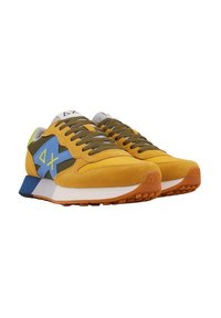 Zapatillas de ante amarillas con acentos en azul y verde, cordones texturizados y una suela blanca con una suela exterior de goma naranja. Logo triangular distintivo.