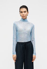 Διαφανές μπλουζάκι μακρυμάνικο σε ανοιχτό μπλε με σχέδιο λεοπάρδαλης; σχέδιο με ψηλό λαιμό. Συνδυάζεται με σκούρες παντελόνες με κορδόνι στη μέση.