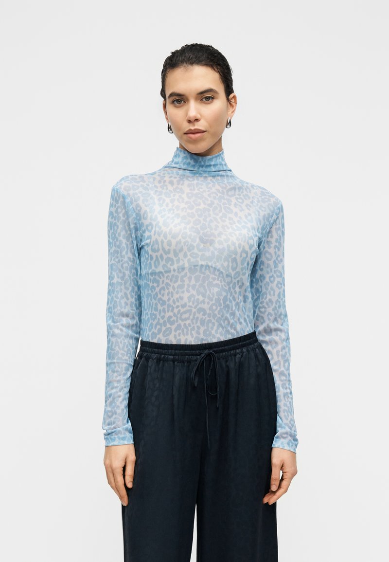 Διαφανές μπλουζάκι μακρυμάνικο σε ανοιχτό μπλε με σχέδιο λεοπάρδαλης; σχέδιο με ψηλό λαιμό. Συνδυάζεται με σκούρες παντελόνες με κορδόνι στη μέση.