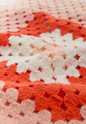 Virkat blanket med växlande sektioner av korall, rosa och vit garn. Den strukturerade, mjuka stygnen i ett geometriskt mönster ökar det visuella intresset.