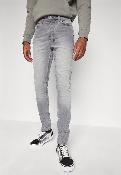 Jeans slim-fit grigi con texture sbiadita, dotati di design classico a cinque tasche, un bottone di chiusura e zone consumate sulle ginocchia. Abbinati a sneakers nere e bianche.