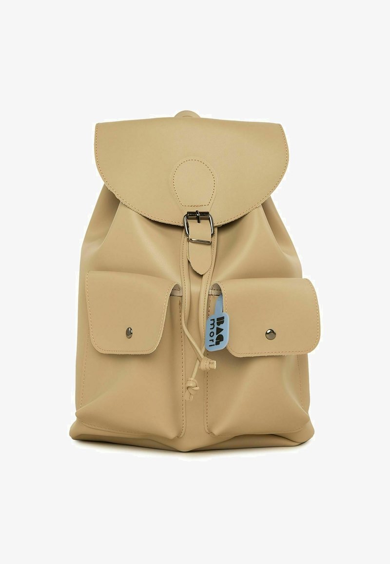 Beež nahast seljakott ümarate klappidega, hõbedaste detailidega ja kahe esikotiga. Omab paelaga sulgemist ja logo silti.